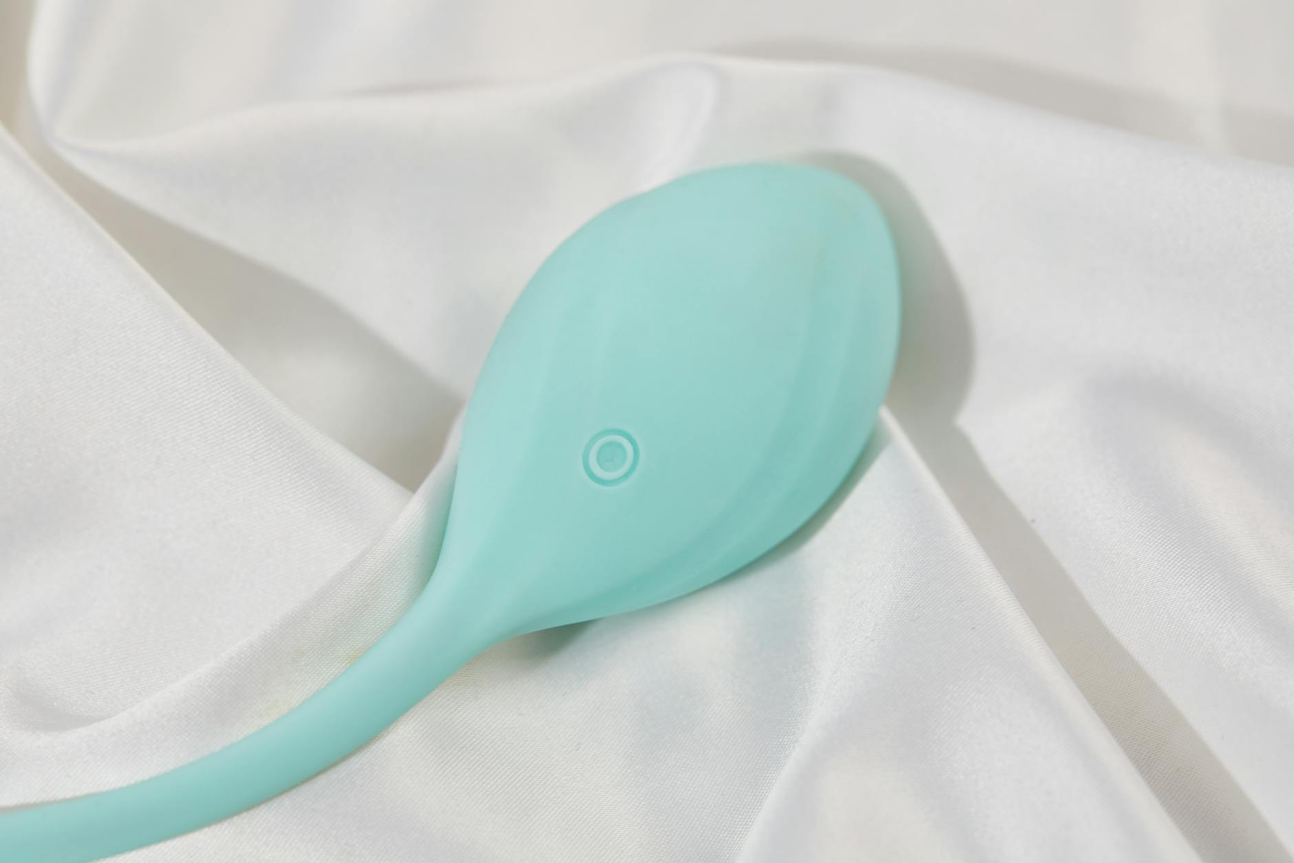 A teal lemon clitoral vibrator on white silk fabric, symbolizing sensitive pleasure