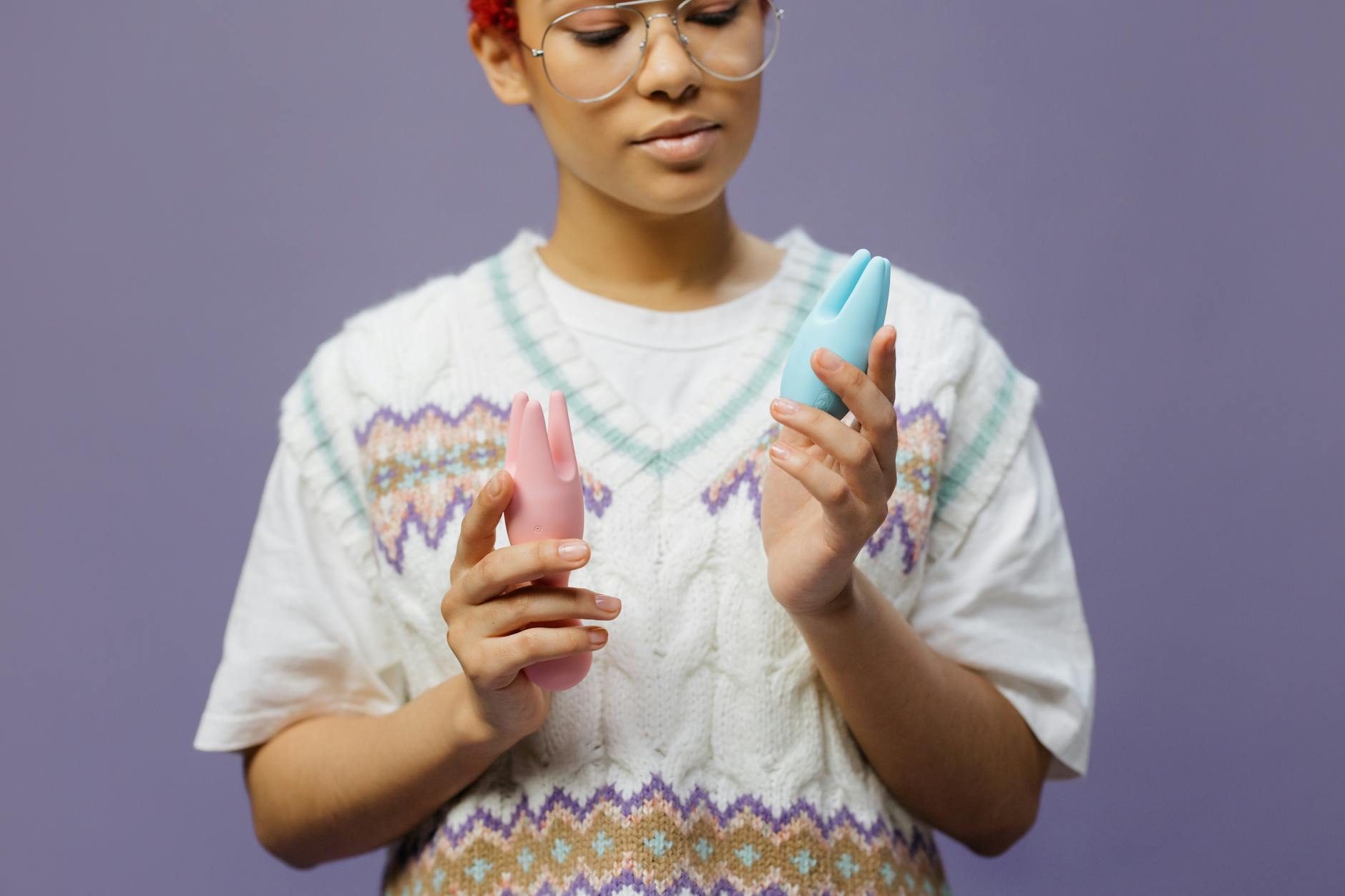 Woman holding blue and pink silicone vibrators in a thoughtful pose.